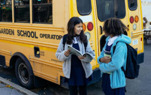 A couple of kids in uniform in front of a school bus.
